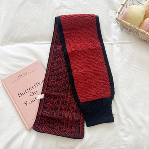 Detailansicht eines rot-schwarzen Strickschals auf weißem Stoff mit warmen Lifestyle-Deko
