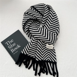 Close-up of winter knit scarf featuring black and white herringbone pattern with fringe