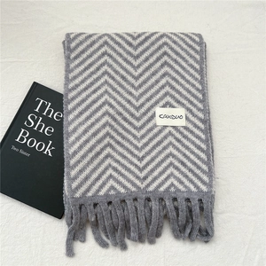 Close-up of knit winter scarf with grey wave pattern, tassels and brand label detail