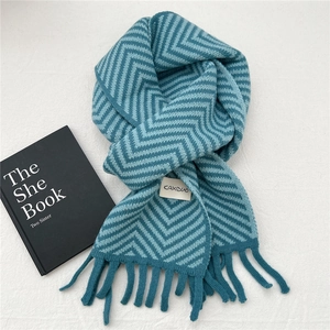 Detail of teal chevron knit scarf featuring fringe ends and a branded woven label