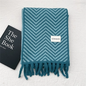 Detail of chevron knit pattern with soft fringe and logo tag on blue and green winter scarf