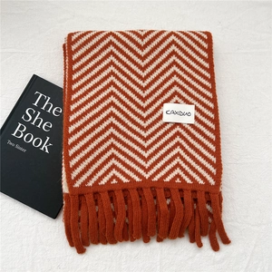 Close-up of orange and white herringbone knit scarf with fringe and brand label