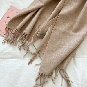 Close-up of camel wool scarf showing soft texture, fringed edges and care label details