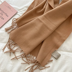 Detail of 100% wool camel scarf texture with fringed edges on a soft fabric backdrop