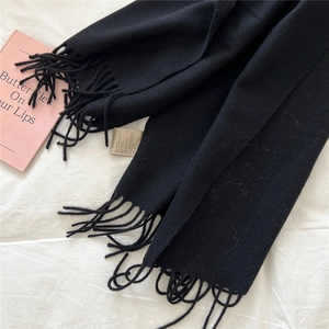 Close-up of black wool scarf with long tassels and care label on white linen fabric