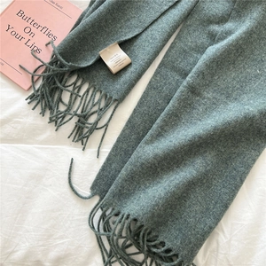 Detailed close-up of blue-green 100% wool scarf with fringe and material care label