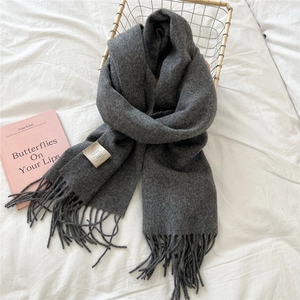 Detail of dark grey 100% wool scarf with handmade fringes on a cozy white bed