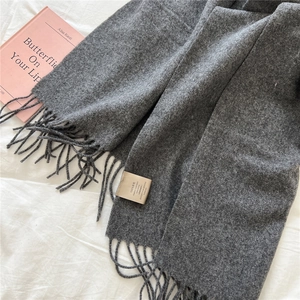 Detailed shot of dark grey wool scarf with tassels and 100% wool material label