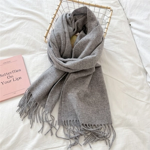 Close-up of light grey wool scarf texture and elegant fringe details in a cozy basket