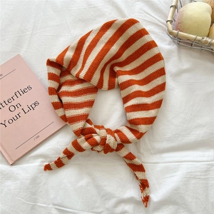 Detail eines orange-weiß gestreiften Strickschals auf weißem Stoffhintergrund