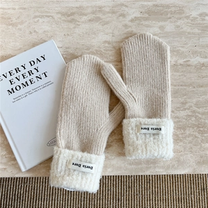 Close-up of beige knitted mittens with plush white faux shearling cuffs and brand label