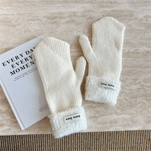 Detail of knitted mittens with fluffy fleece cuffs and minimalist fabric brand label