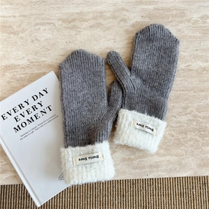 Detailed texture of gray knit mittens with white fluffy cuffs and fabric logo label