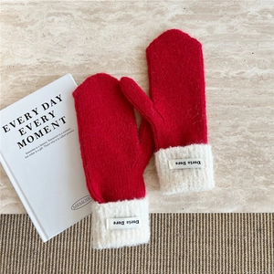 Close-up of red knit mittens with white plush cuffs and Doria Dore logo label on tabletop