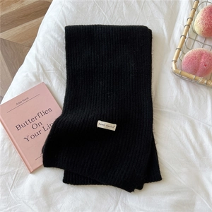 Detail of black ribbed knit scarf featuring white woven label on soft white texture