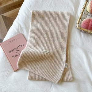 Detail of chunky ribbed knit scarf in beige with a minimalist woven brand tag