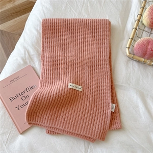 Close-up of pink chunky knit scarf with fabric brand label on a soft bed background