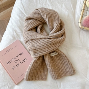 Detailed texture of beige rib-knitted winter scarf with brand tag on soft fabric background