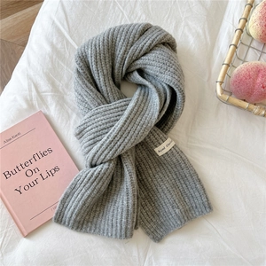 Close-up of light gray chunky knit scarf with thick ribbed texture and woven brand label
