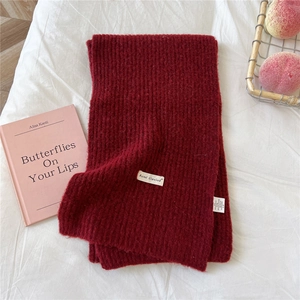 Close-up of deep burgundy knit scarf texture with brand label on soft white fabric