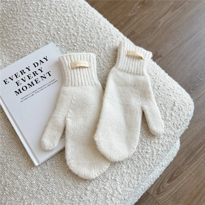 Detailed texture of thick cream wool mittens with 100% wool label on soft faux fur