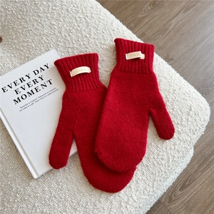 Detail of red 100% wool knitted mittens with ribbed cuffs on a soft textured background