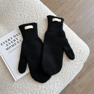Close-up of black 100% wool knitted mittens with ribbed cuffs on soft boucle fabric