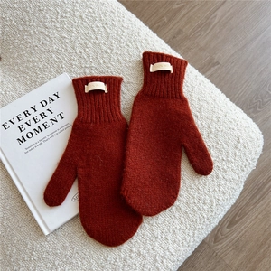 Detail of 100% wool label on brick red knitted mittens for winter warmth and comfort