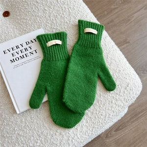 Detailed knit texture of green wool mittens with a 100% wool label on soft fleece