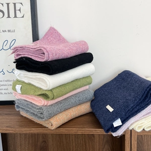Stack of multi-colored knit scarves showing thick woolen texture on a wooden desk
