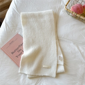 Detailed view of cream white knitted scarf with leather brand label on soft white linen