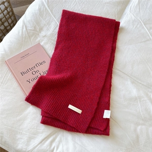 Detail of red knitted scarf with vertical rib texture and silver metal brand tag