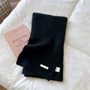 Close-up of black ribbed knit scarf featuring a soft texture and brand logo detail