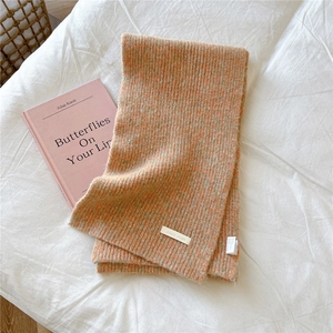 Detail of warm orange ribbed knit scarf with soft texture and white brand logo label