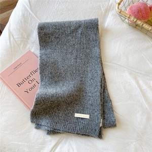 Detail of thick grey knit scarf with woven logo label on soft white fabric background