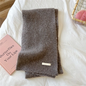 Detail of soft brown ribbed knit scarf with a decorative white woven label on fabric
