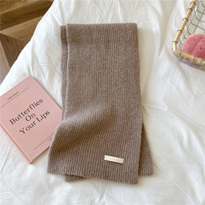 Close-up of brown knit scarf with fine ribbed texture and silver metal brand plate