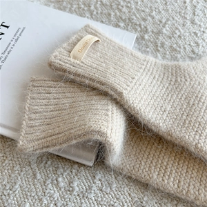 Detailed texture of thick beige knit gloves showing plush mohair and brand label