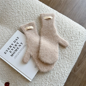 Close-up of beige knitted mittens with Doria Dore label on a soft textured background