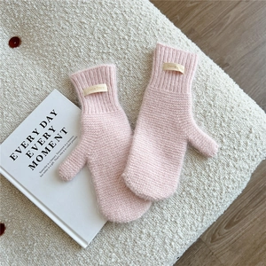 Detail of light pink knitted mittens with brand label on soft white fabric background