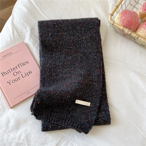 Close-up of thick knitted scarf with colorful speckles and woven brand label detail