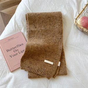 Detail of a chunky knit brown scarf with colorful flecks and a white brand label