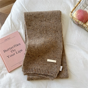 Detail of brown chunky knit scarf with orange specks and brand woven label on white fabric