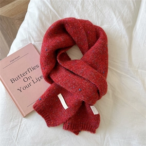 Detail of red tweed knit scarf featuring rainbow specks and brand label on white fabric