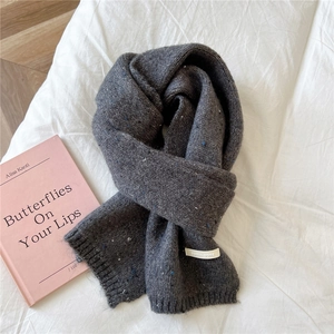 Detailed texture of dark grey knit scarf with blue specks and white woven label