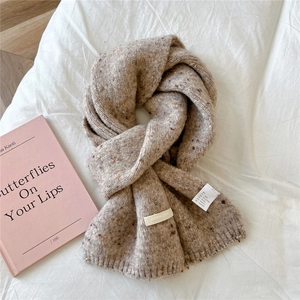 Detailed knit texture of long wool blend scarf with colorful flecks on a white surface