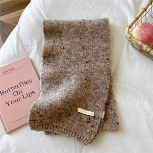 Detailed texture of thick knitted scarf with colorful flecks and woven label on white fabric