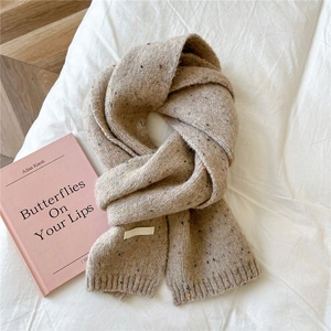 Close-up of beige knit scarf with colorful nep yarn texture and ribbed edge on white bed