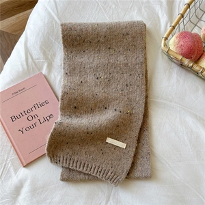 Detail of light brown knit scarf with rainbow flecks and brand label on white bedding