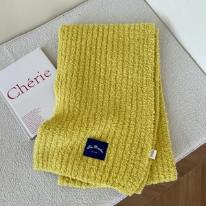 Detailed view of yellow chunky knit scarf with woven brand label on a textured bench